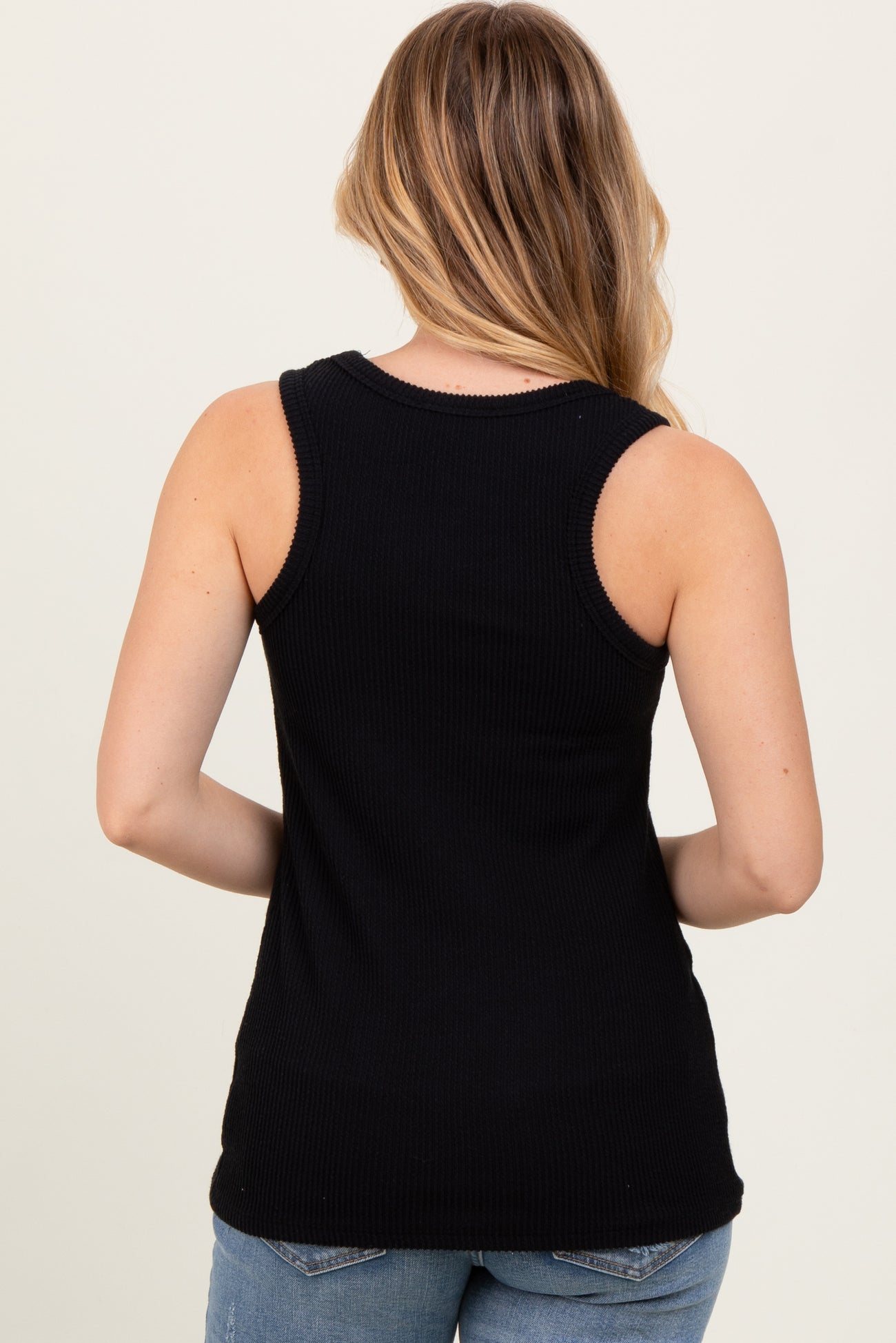 woman wearing a black ribbed tank top seen from the back with long hair and casual denim jeans