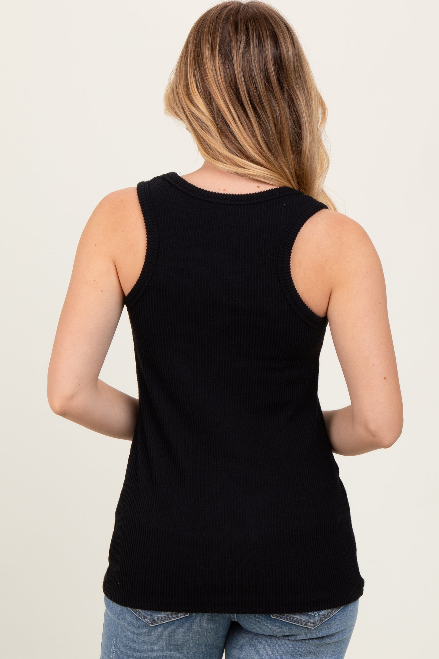 woman wearing a black ribbed tank top seen from the back with long hair and casual denim jeans