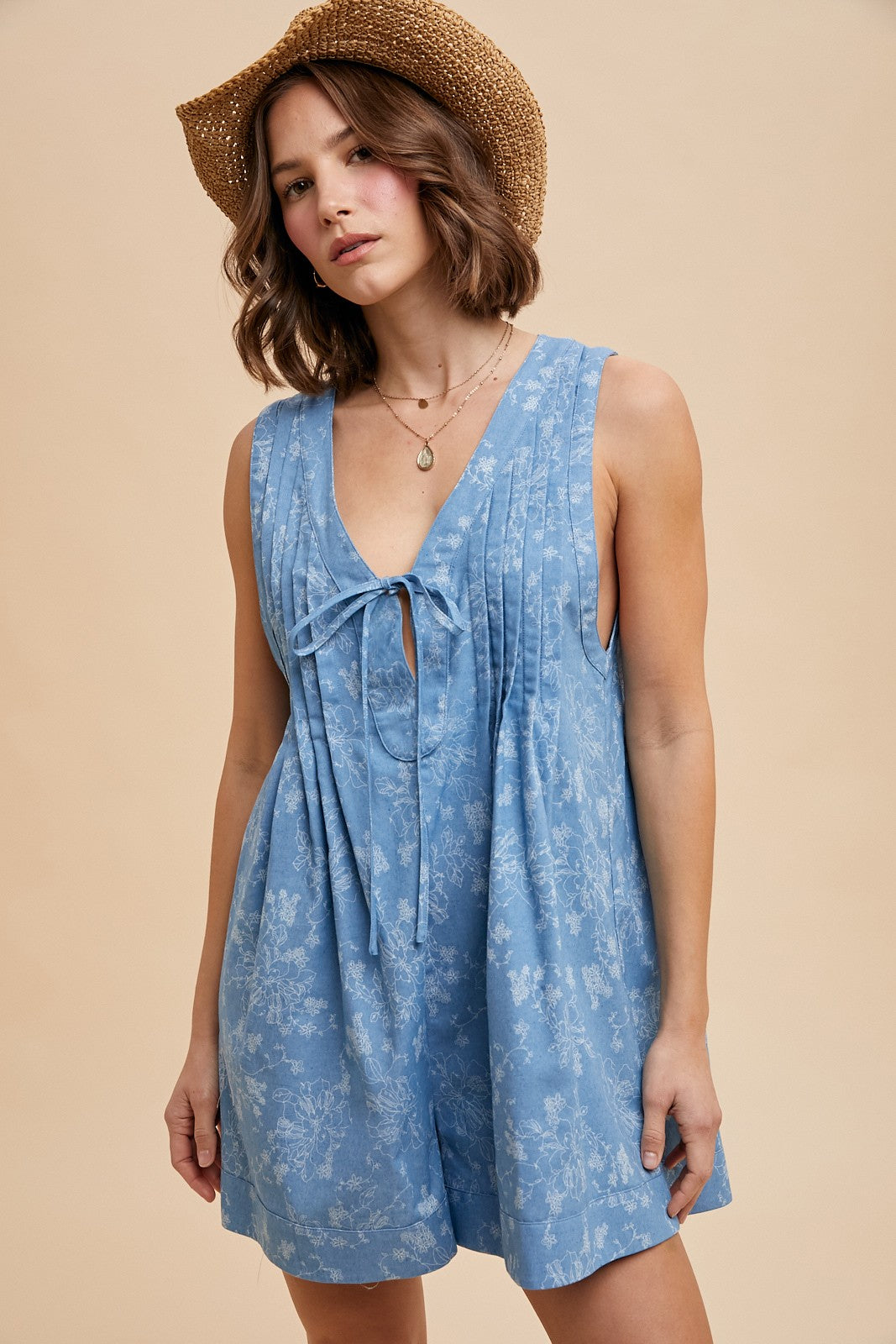 woman wearing a light blue floral sleeveless romper with a tie front detail and a straw hat