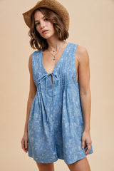 woman wearing a light blue floral sleeveless romper with a tie front detail and a straw hat