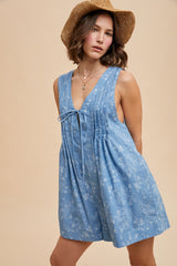 woman wearing a blue floral print sleeveless romper with a tie detail and a straw hat