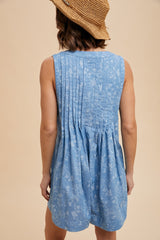 woman wearing a light blue sleeveless dress with back pleats and floral pattern, turned away from the camera