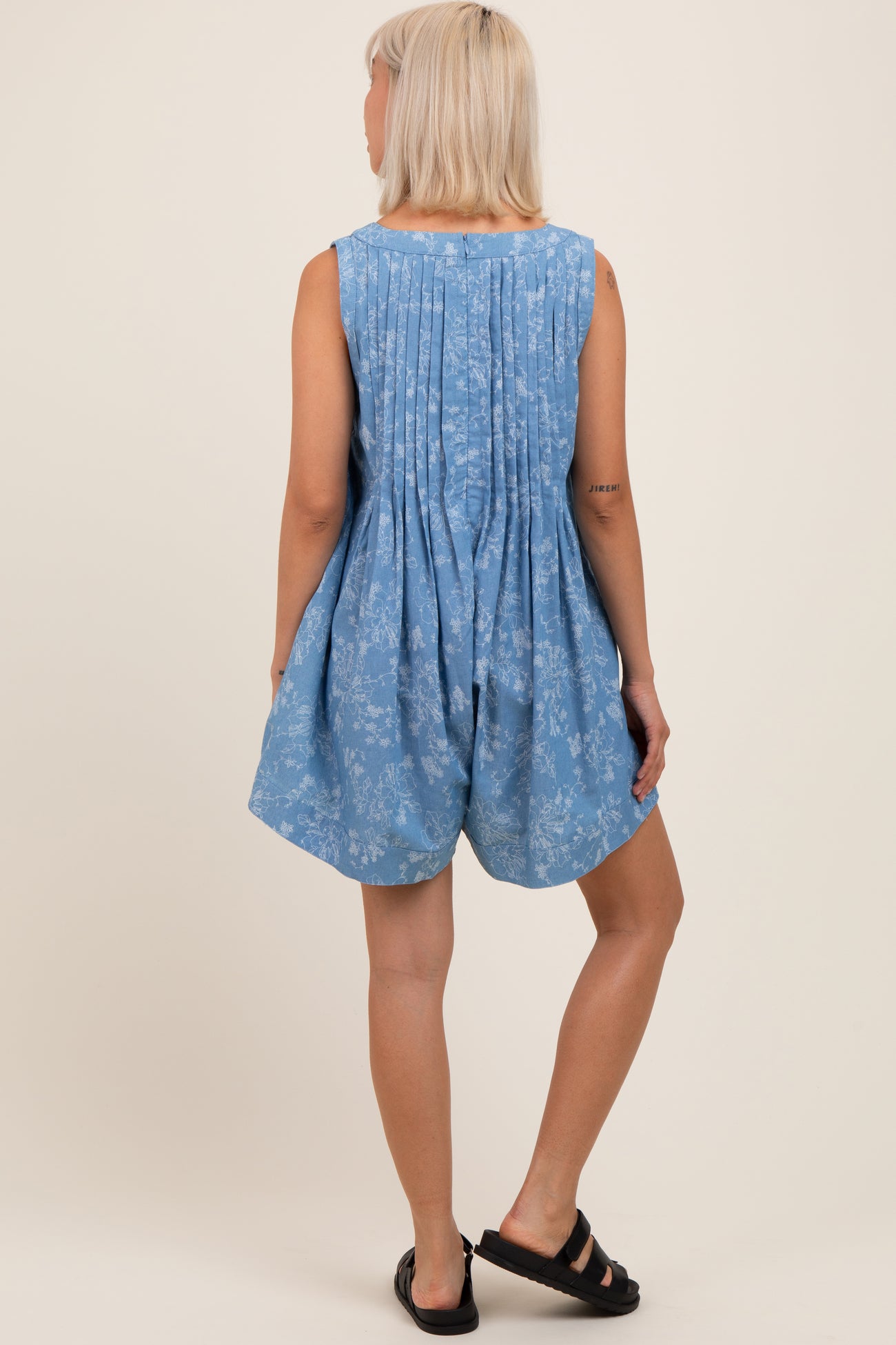 woman wearing a light blue maternity romper with a floral pattern and pleated back detail