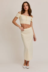 woman wearing a cream off-the-shoulder crop top and a matching long skirt, styled with white shoes