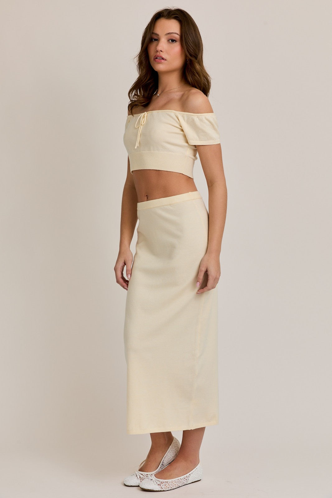 woman wearing a cream cropped off-shoulder top and a matching long skirt, styled with white ballet flats