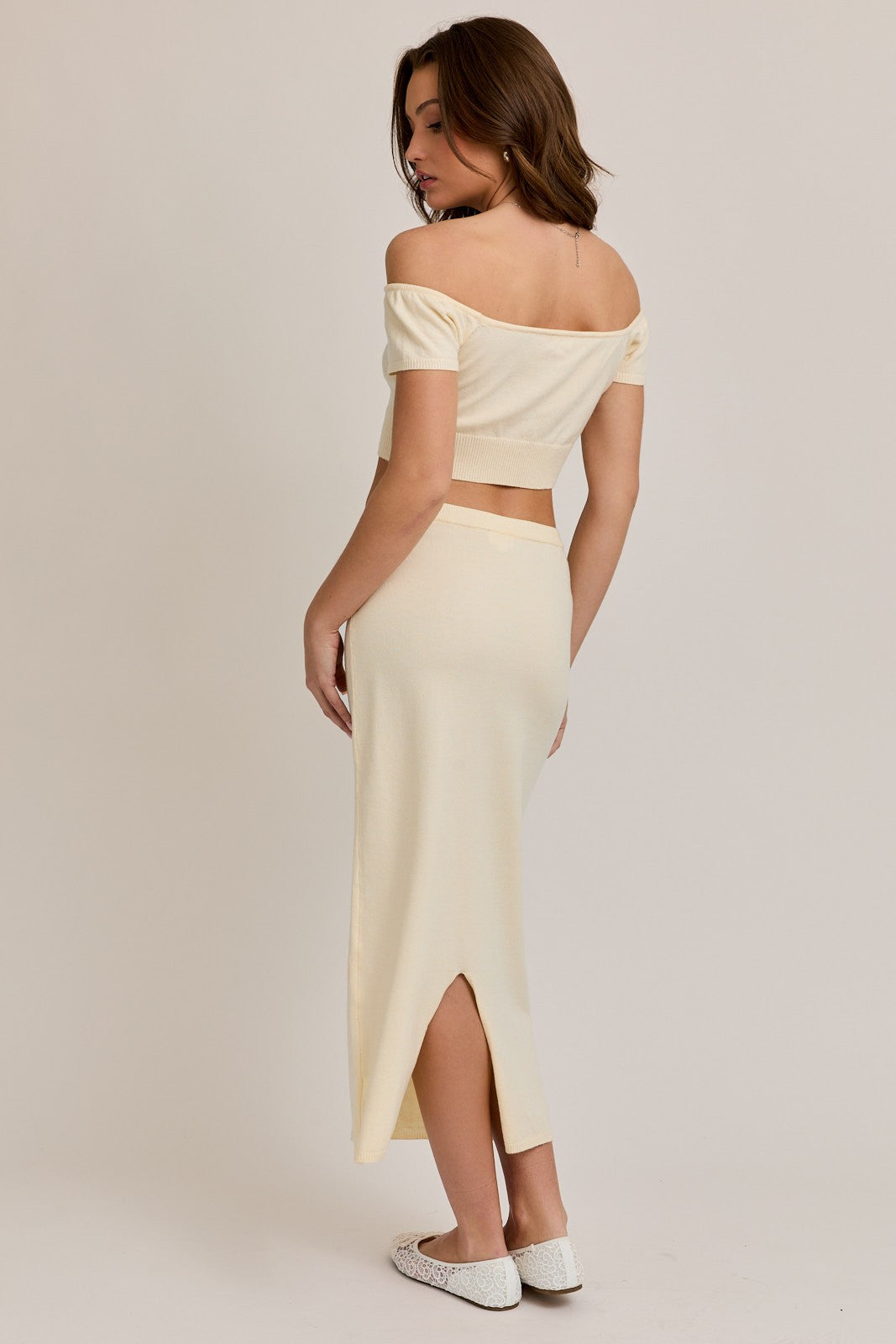 woman wearing a beige off-the-shoulder crop top and a matching midi skirt with a side slit