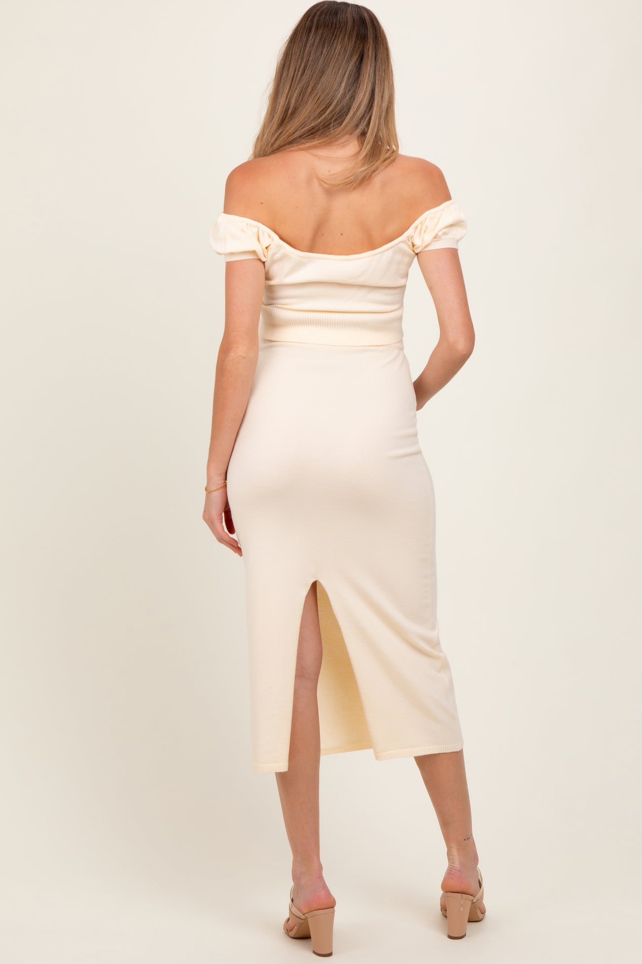 woman wearing a cream off-the-shoulder maternity dress with puff sleeves and a back slit