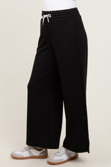 woman wearing black wide-leg sweatpants with an elastic waistband and side slits, paired with white sneakers