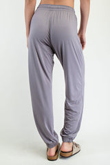 woman wearing gray loose-fitting jogger pants with an elastic waistband and gathered cuffs, viewed from the back