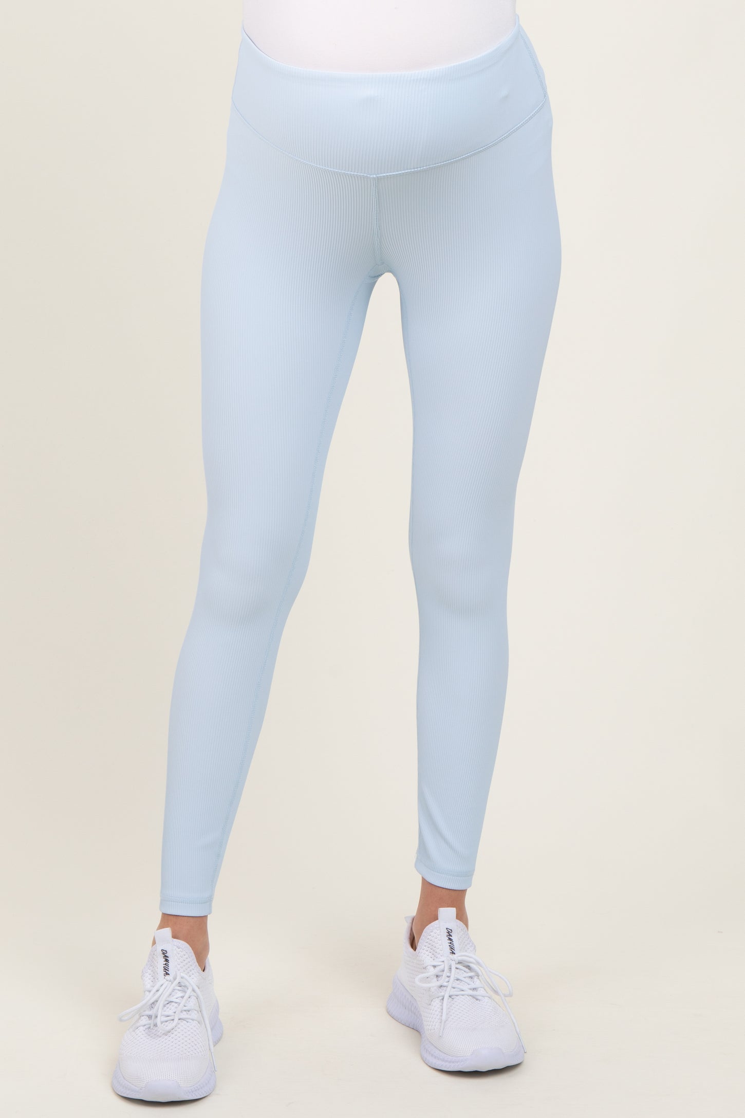 woman wearing light blue maternity leggings with a ribbed texture and a supportive waistband, paired with white athletic shoes