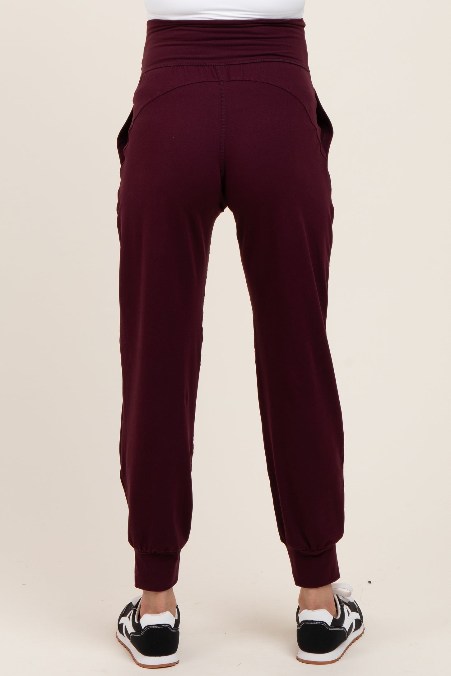woman wearing burgundy maternity joggers with a high waistband and side pockets, viewed from the back