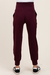 woman wearing burgundy maternity joggers with a high waistband and side pockets, viewed from the back