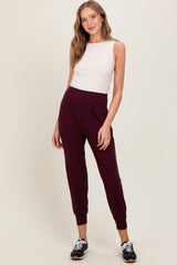 woman wearing a fitted white sleeveless top and burgundy jogger pants with elastic cuffs and waistband