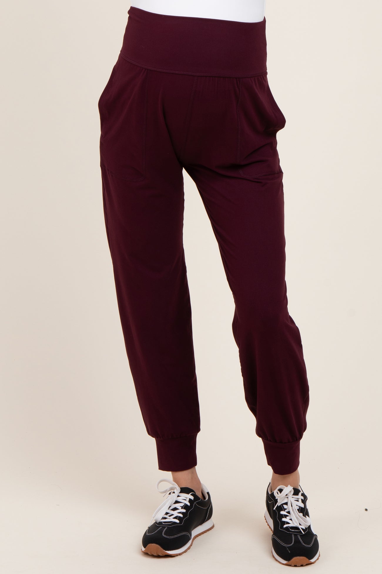 woman wearing burgundy maternity joggers with a wide waistband and tapered cuffs, styled with sneakers