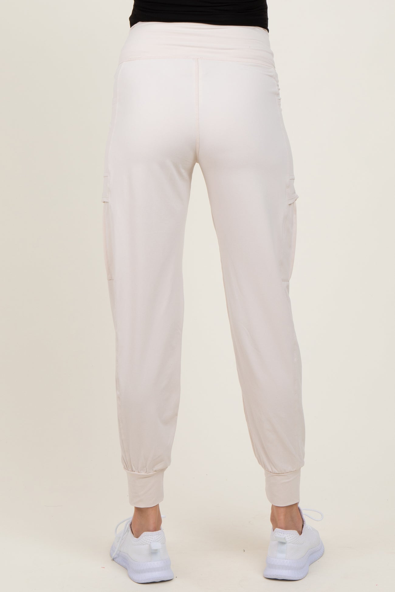 woman wearing light pink maternity cargo pants, showing the back view with elastic waistband and cuffed hems