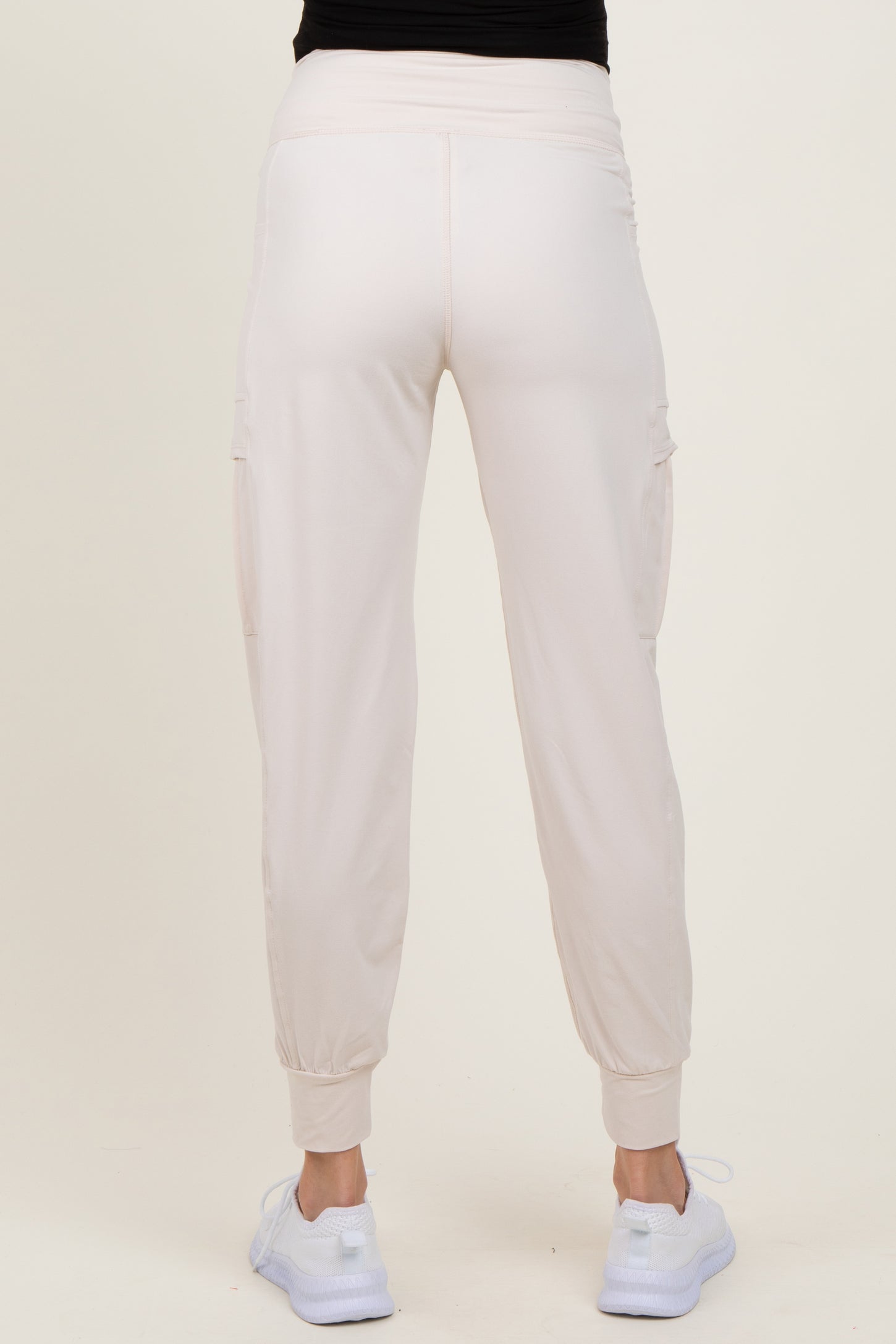 woman wearing light pink maternity cargo pants, showing the back view with elastic waistband and cuffed hems