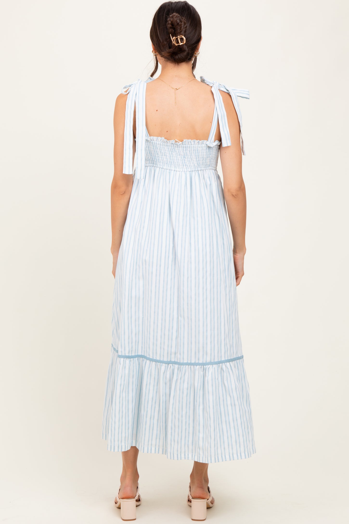 woman wearing a light blue and white striped maxi dress with tie shoulder straps and a ruffled hem