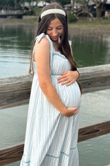 woman wearing a striped maternity dress with tie straps and cradling her baby bump by the water