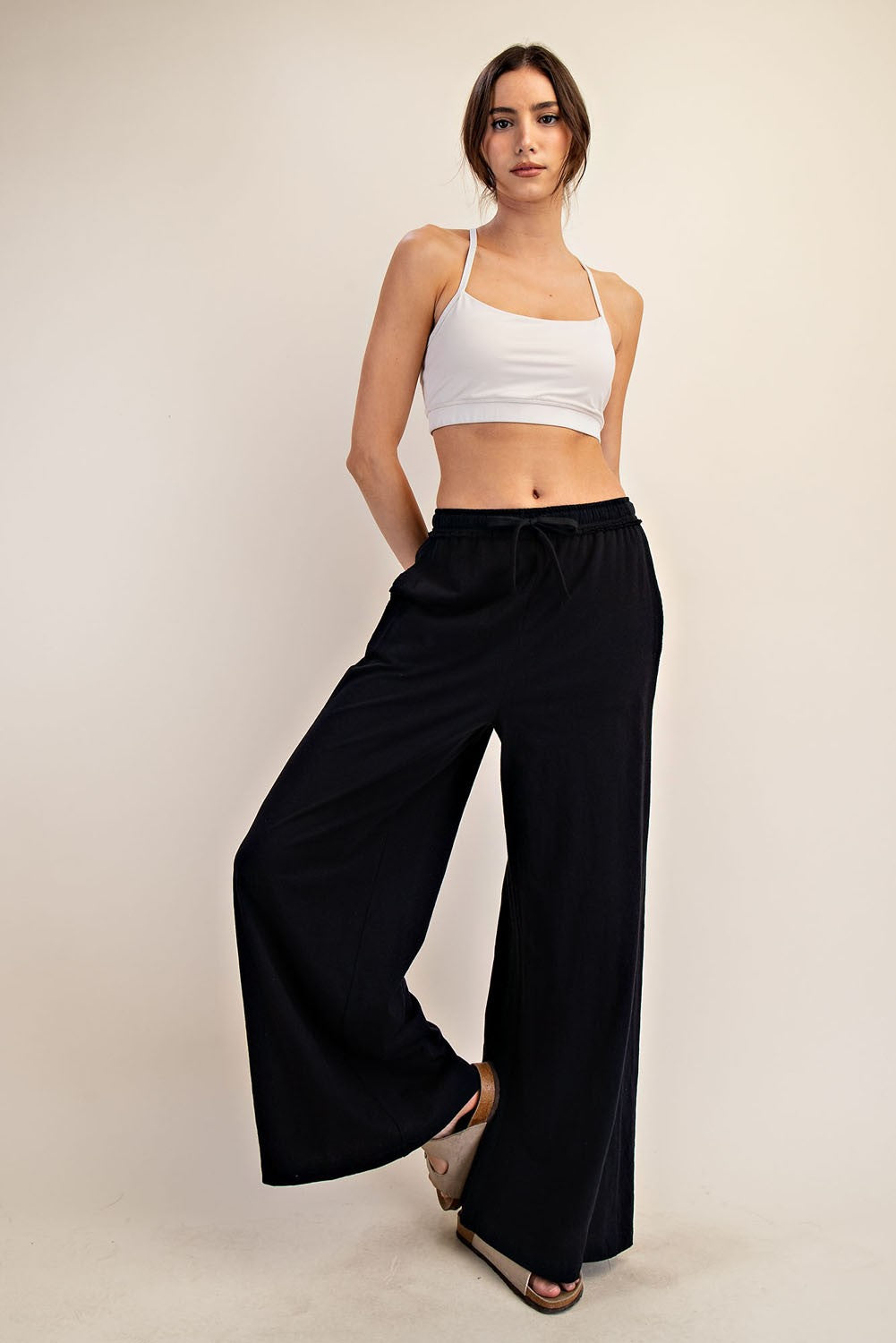 woman wearing a white cropped tank top and black wide leg pants, standing with one leg slightly bent