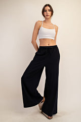 woman wearing a white cropped tank top and black wide leg pants, standing with one leg slightly bent