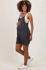 woman wearing a dark gray striped maternity romper with pockets, gently cradling her baby bump
