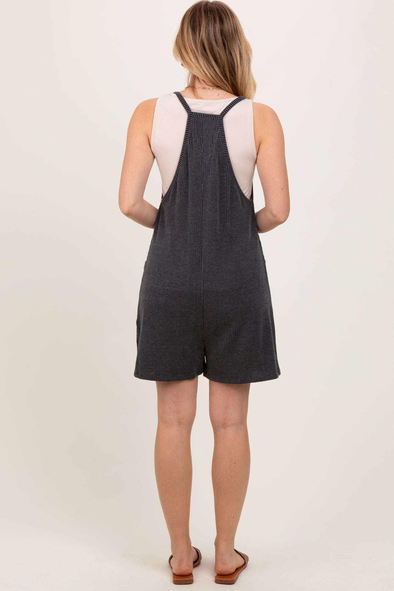 woman wearing a gray striped overall romper with a sleeveless top and back straps, standing with her back to the camera