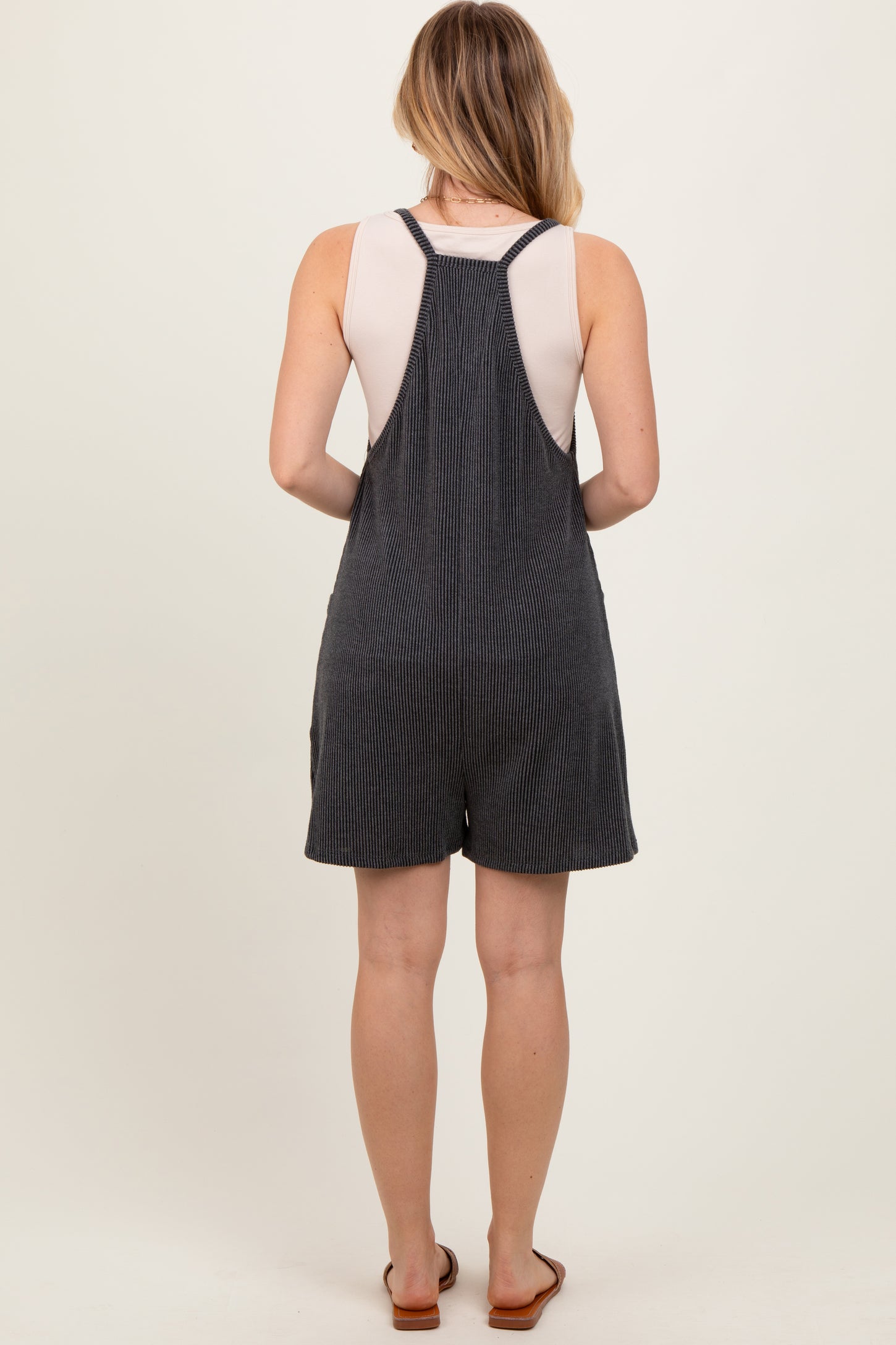 woman wearing a gray striped overall romper with a sleeveless top and back straps, standing with her back to the camera