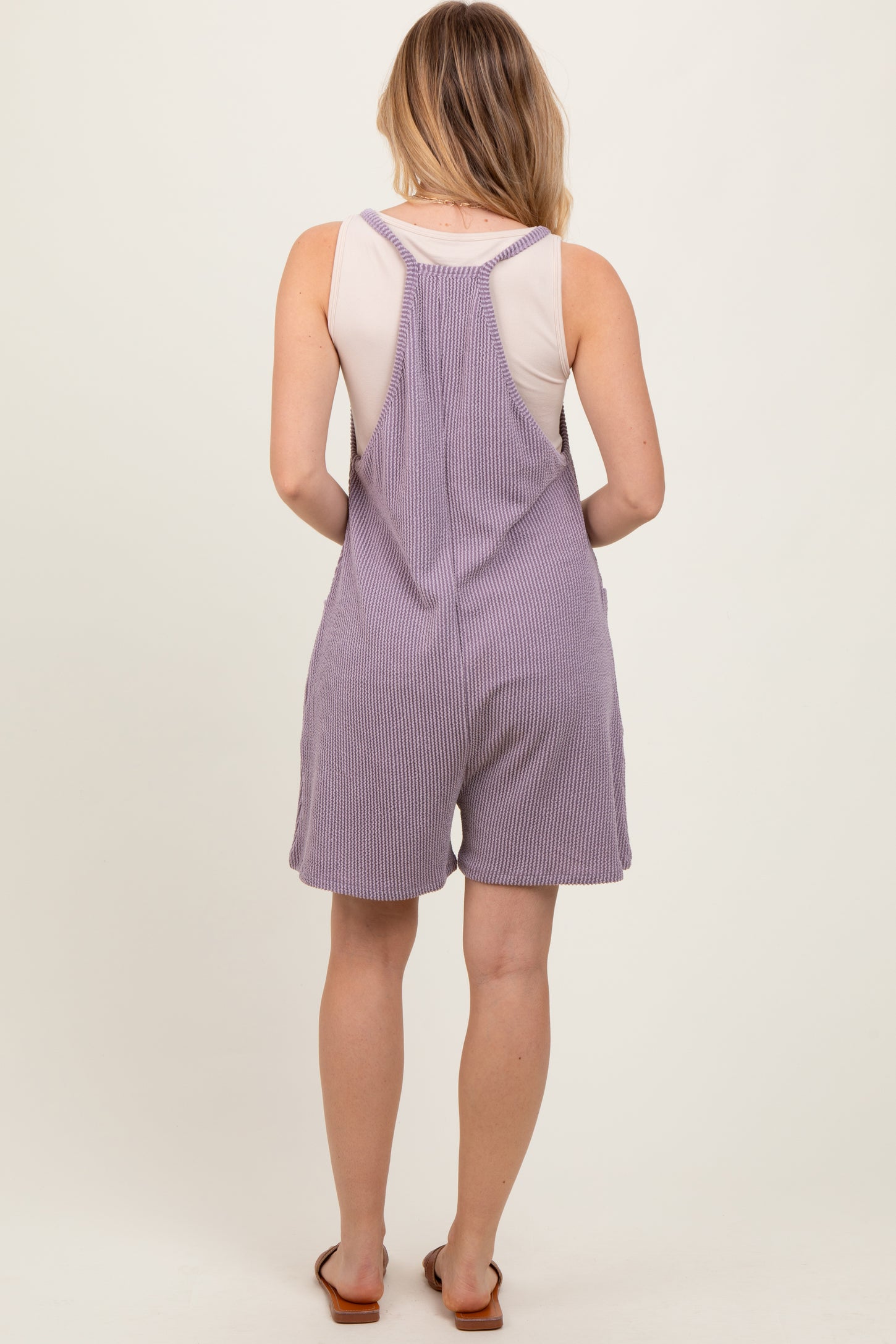 woman wearing a lavender striped romper with a racerback design and shorts length, viewed from the back