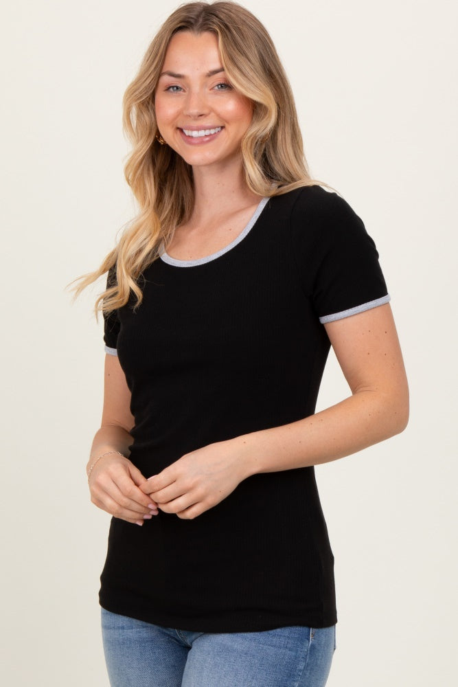 woman wearing a black short sleeve ribbed top with gray trim, smiling and standing with hands clasped in front