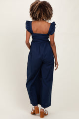 woman wearing a navy blue maternity jumpsuit with smocked bodice and ruffle sleeves, seen from the back