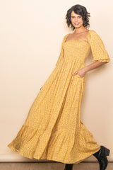 woman wearing a yellow floral maxi dress with a square neckline and short bell sleeves, posing confidently
