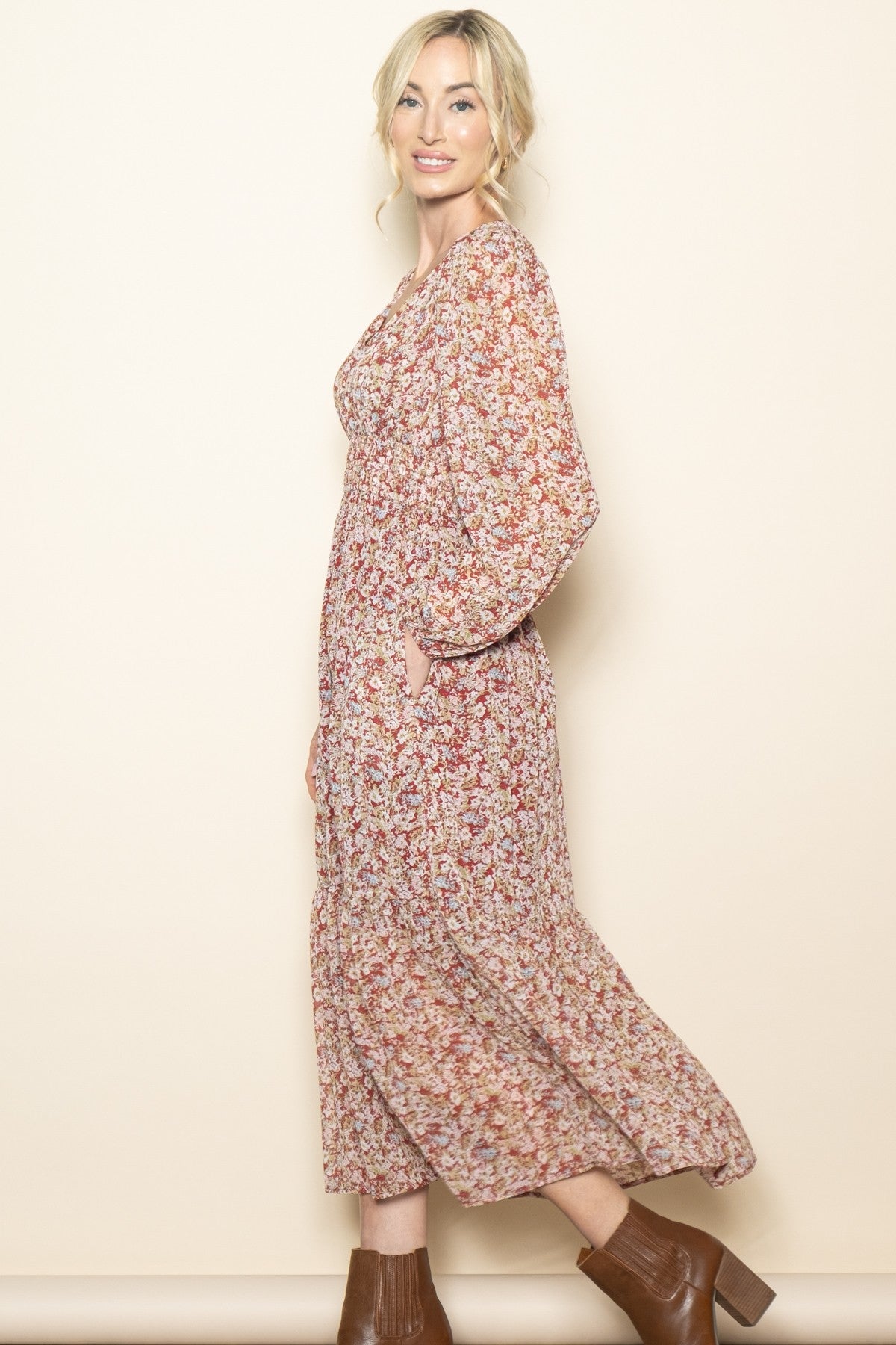 woman wearing a floral maxi dress with long sleeves and pockets, smiling against a neutral background