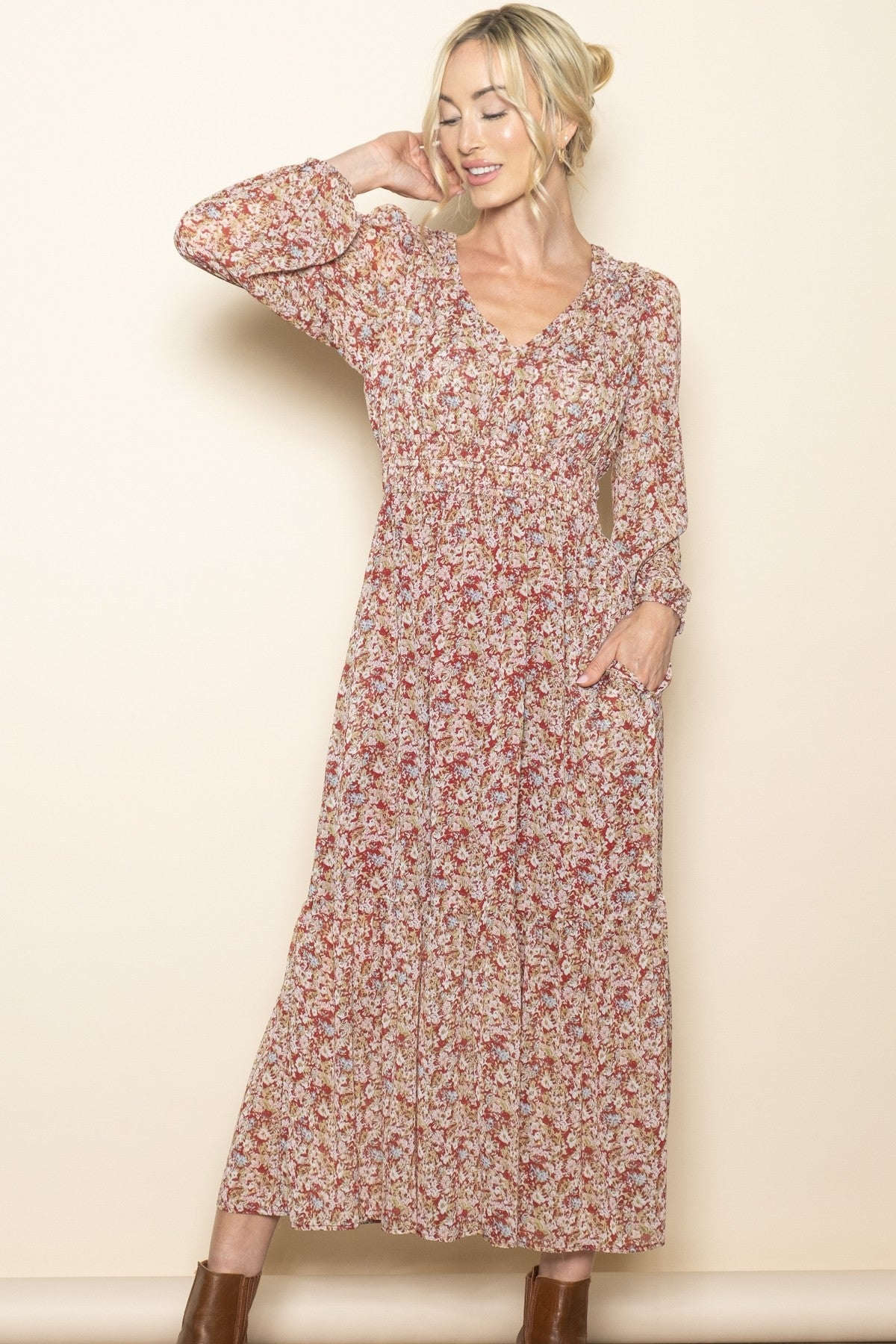 woman wearing a long floral print maxi dress with long sleeves and pockets, smiling against a neutral background