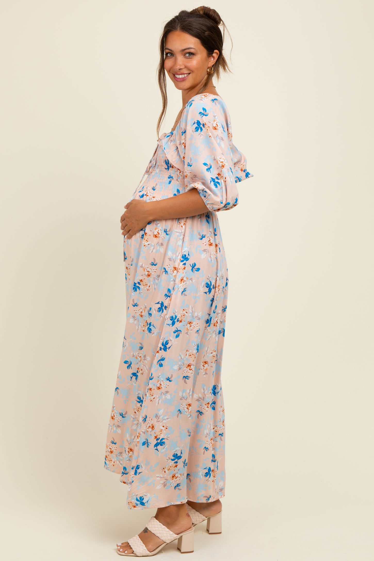 woman wearing a light pink floral maternity maxi dress and holding her baby bump