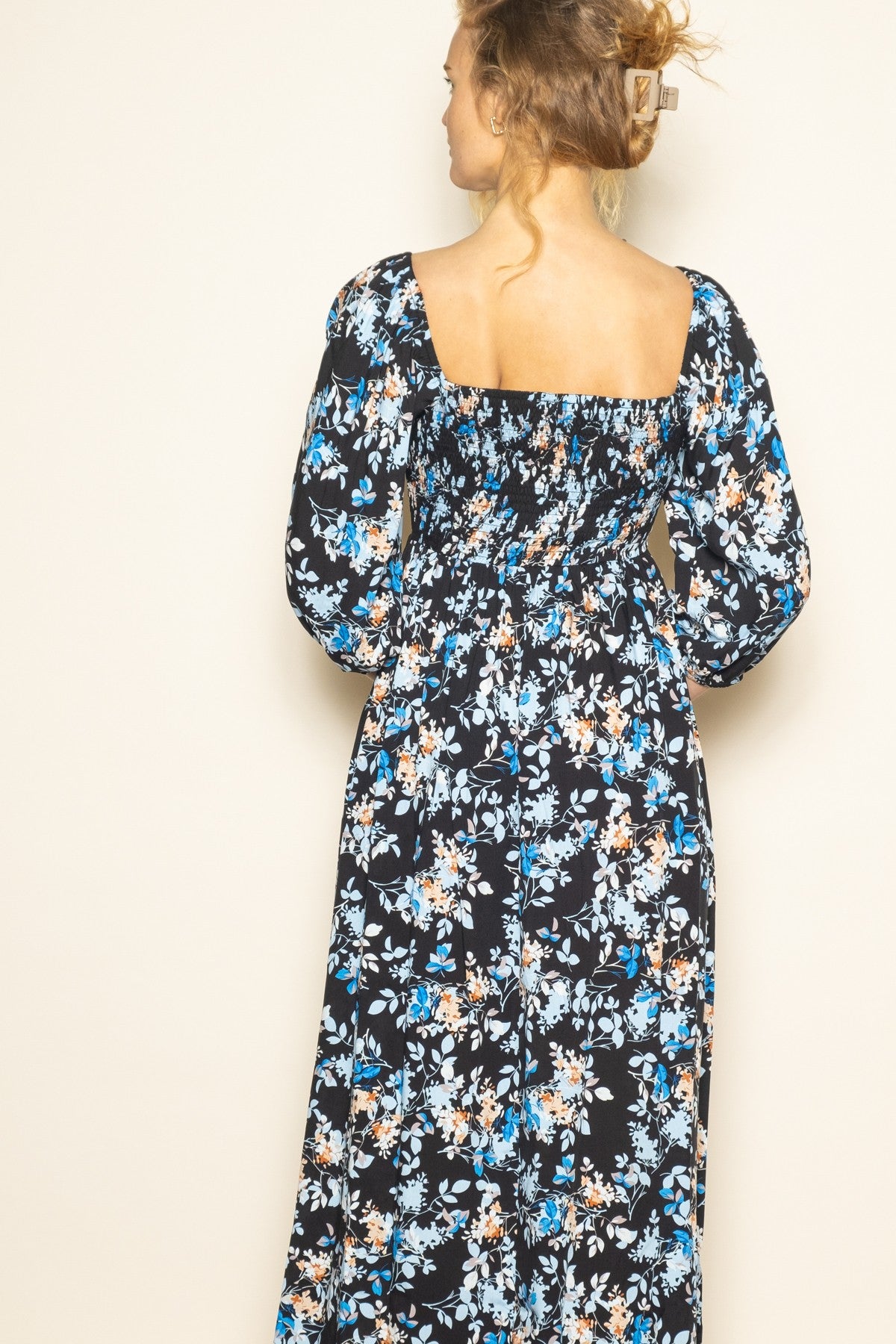 woman wearing a black floral maxi dress with puff sleeves and a fitted waist, view from the back