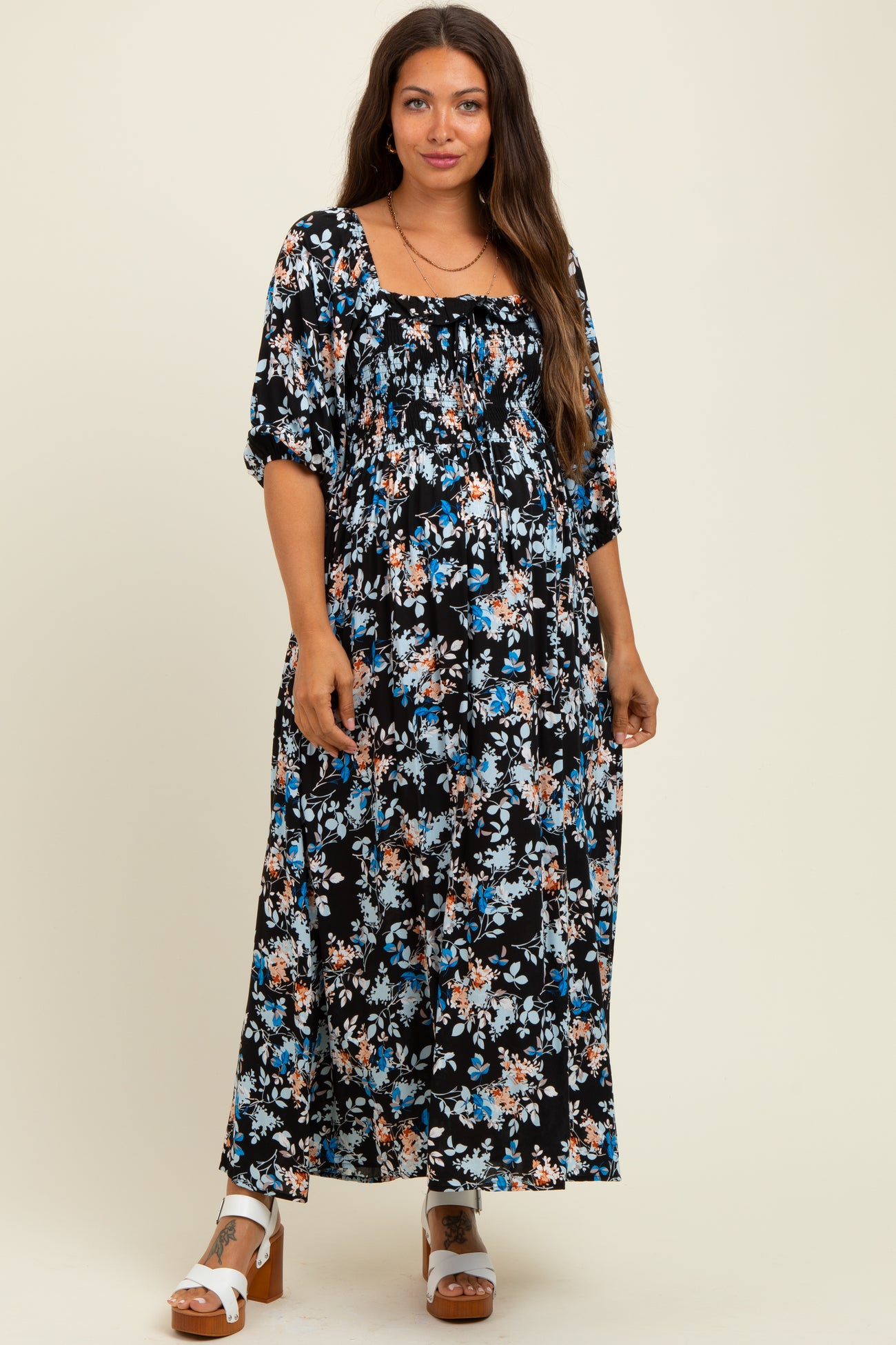 woman wearing a black floral maternity maxi dress with short puff sleeves and a gathered neckline, showcasing her baby bump