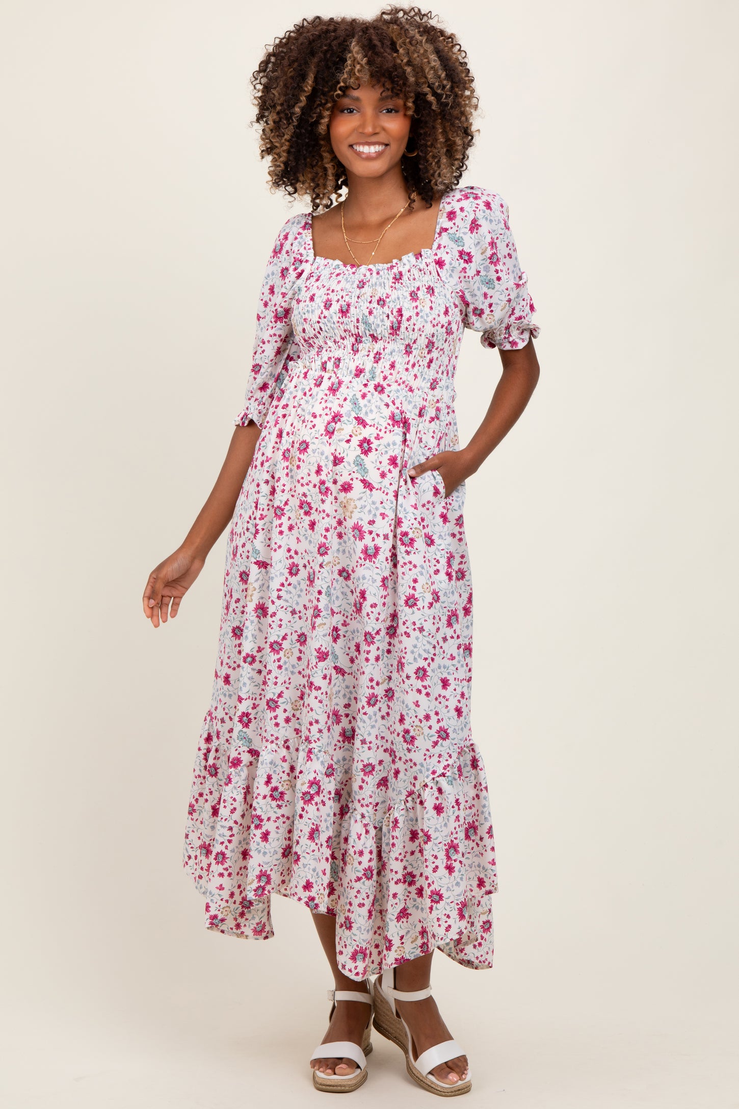 woman wearing a floral print maternity dress with a smocked bodice, ruffled hem, and pockets, featuring a visible baby bump