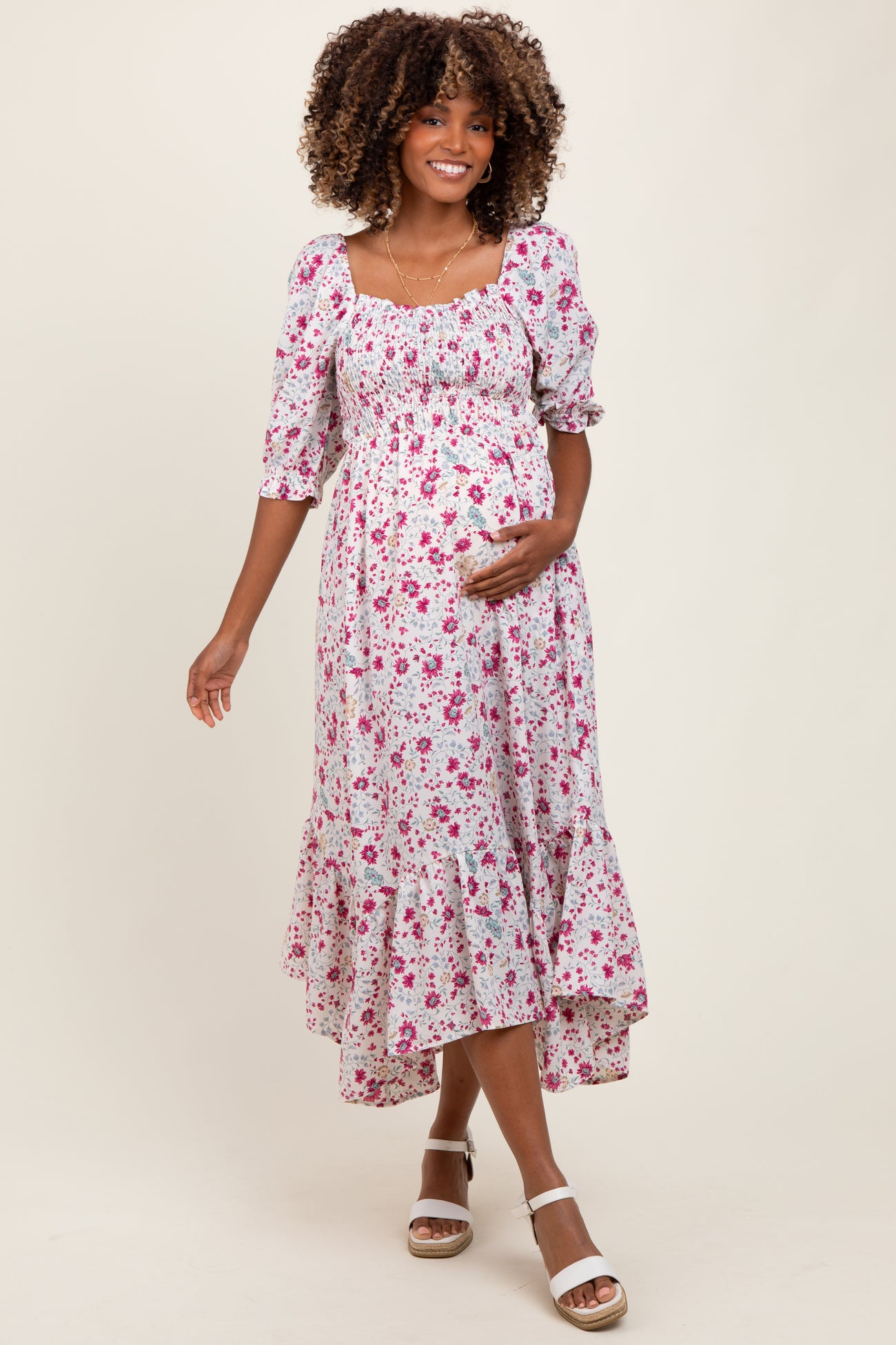 woman wearing a floral print maternity dress with a square neck, puff sleeves, and a flowing skirt, holding her baby bump