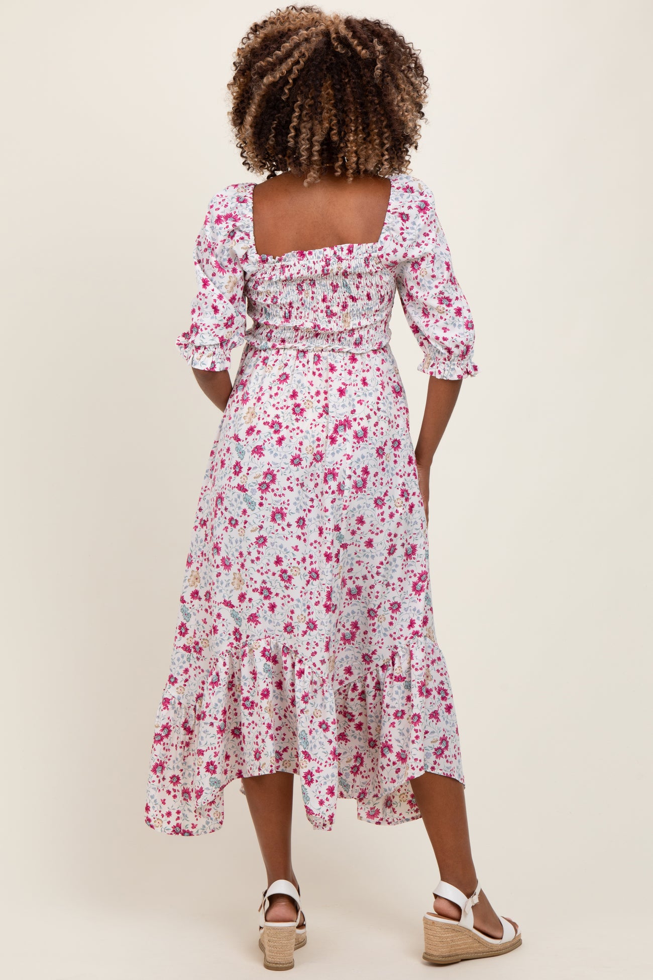 woman wearing a floral print maternity dress with smocked details and ruffled hem, showing a baby bump from the back