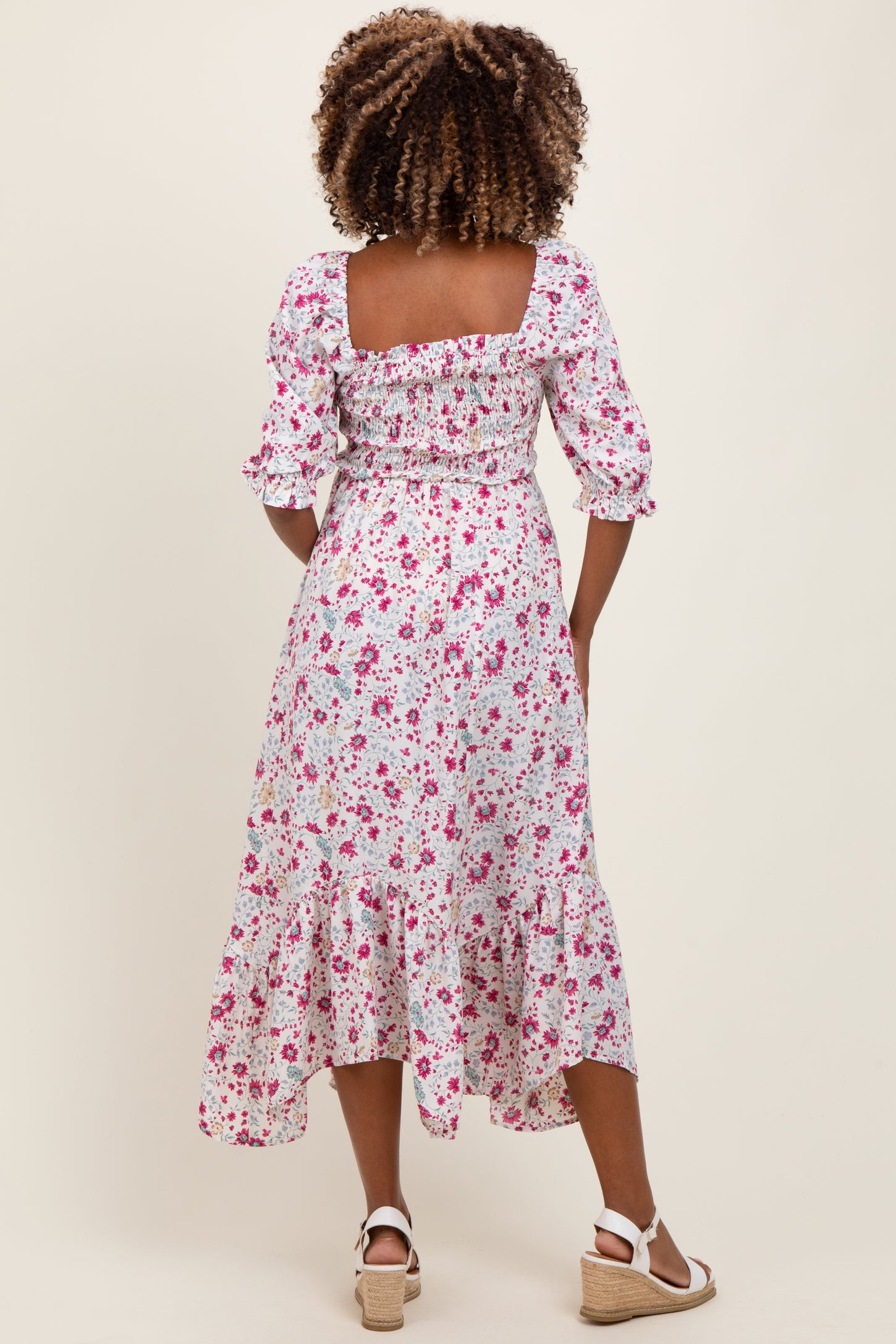 woman wearing a floral print maternity dress with smocked details and ruffled hem, showing a baby bump from the back