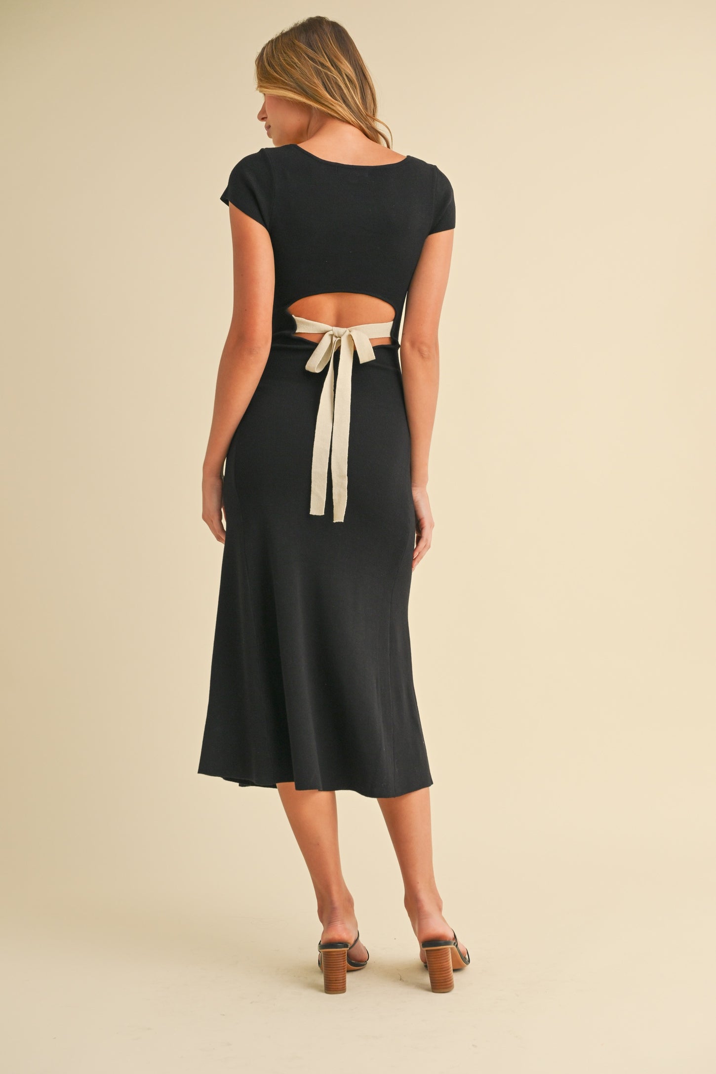 woman wearing a black midi dress with a cutout back and tie detail, styled with heels