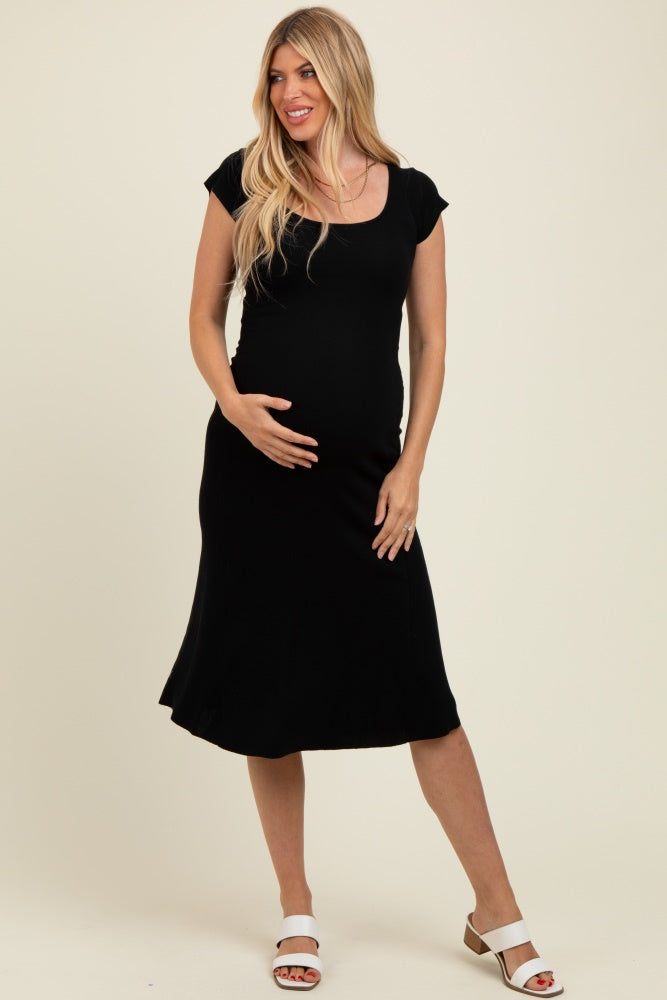 woman wearing a black maternity dress with short sleeves and a flowing skirt, gently holding her baby bump