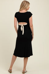 woman wearing a black maternity dress with a back cutout and tie detail, highlighting her baby bump