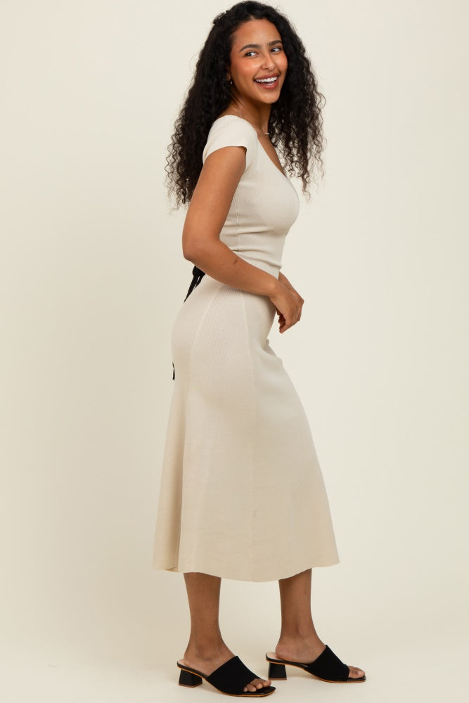 woman wearing a beige ribbed midi dress with cap sleeves and a tie detail at the waist, smiling and standing sideways
