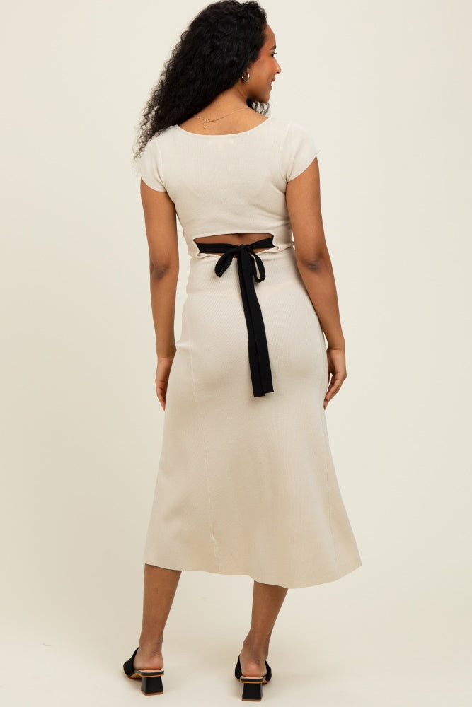 woman wearing a beige two-piece dress with a cutout back and a black tie detail, standing against a neutral background