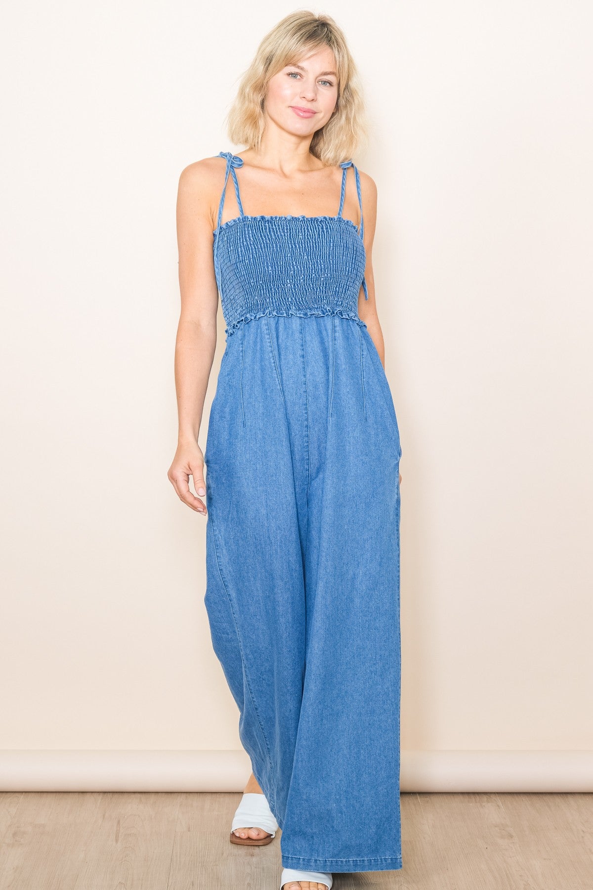 woman wearing a light blue denim jumpsuit with smocked bodice and adjustable straps