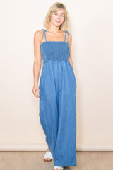 woman wearing a light blue denim jumpsuit with smocked bodice and adjustable straps