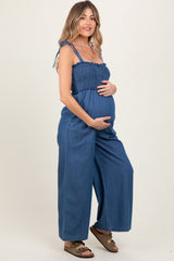 woman wearing a blue smocked maternity jumpsuit and cradling her baby bump