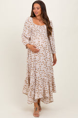 woman wearing a floral print maternity maxi dress with a smocked bodice and tiered hem, gently cradling her baby bump