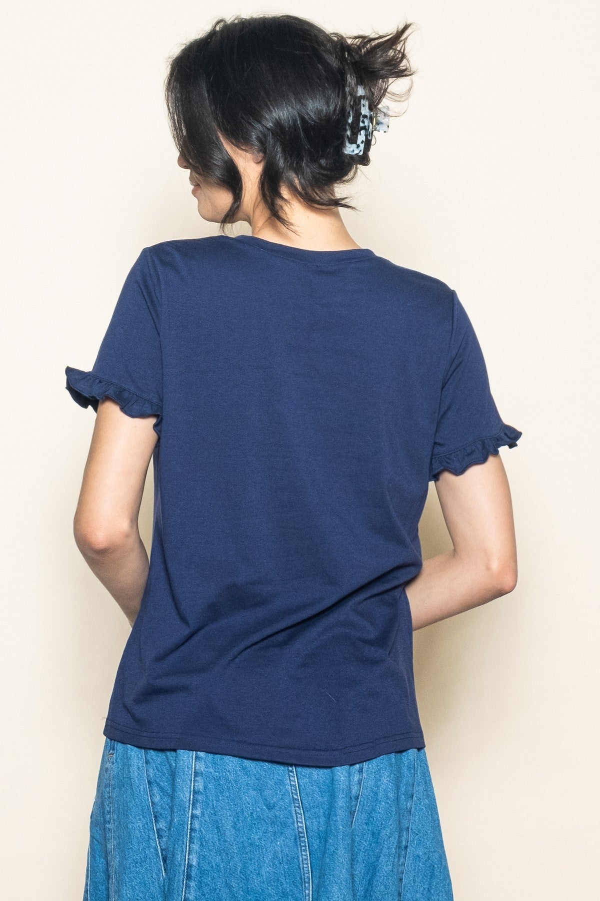 woman wearing a navy blue short sleeve t-shirt with ruffle details and a denim skirt